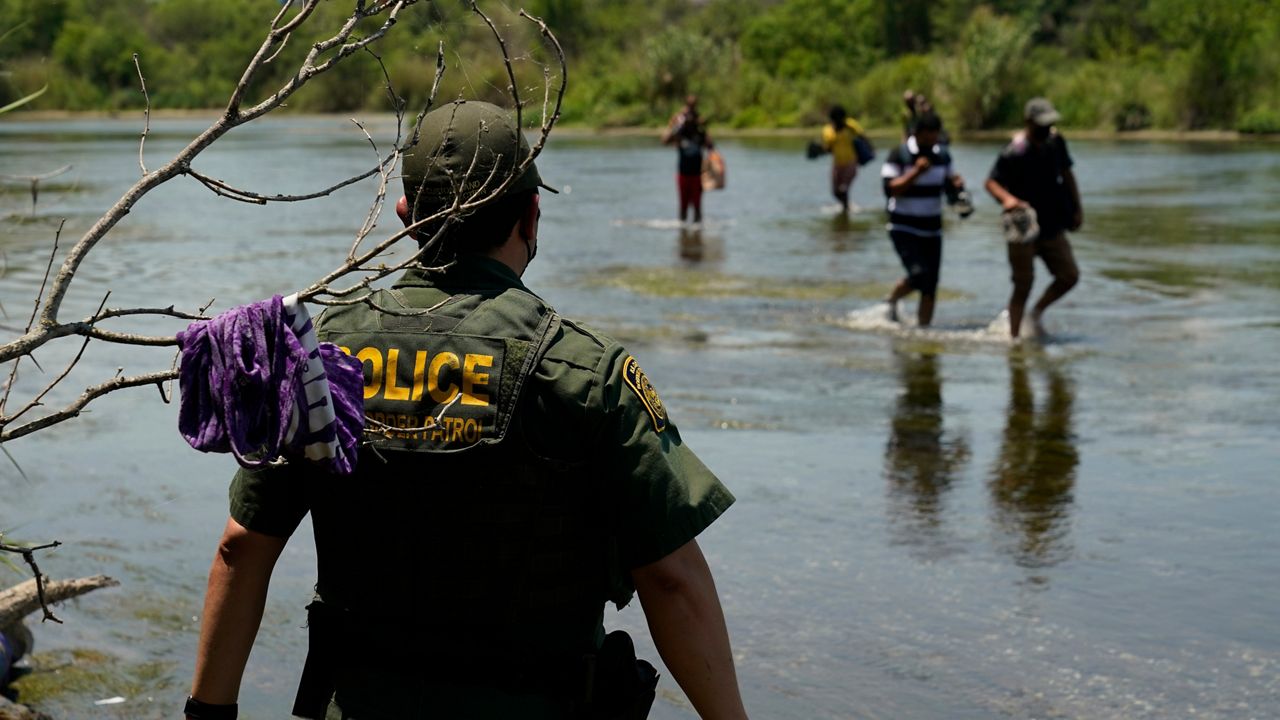 In this June 15, 2021, file photo, a Border Patrol agent watches as a group of migrants walk across the Rio Grande on their way to turning themselves in upon crossing the U.S.-Mexico border in Del Rio, Texas. (AP Photo/Eric Gay, File)
