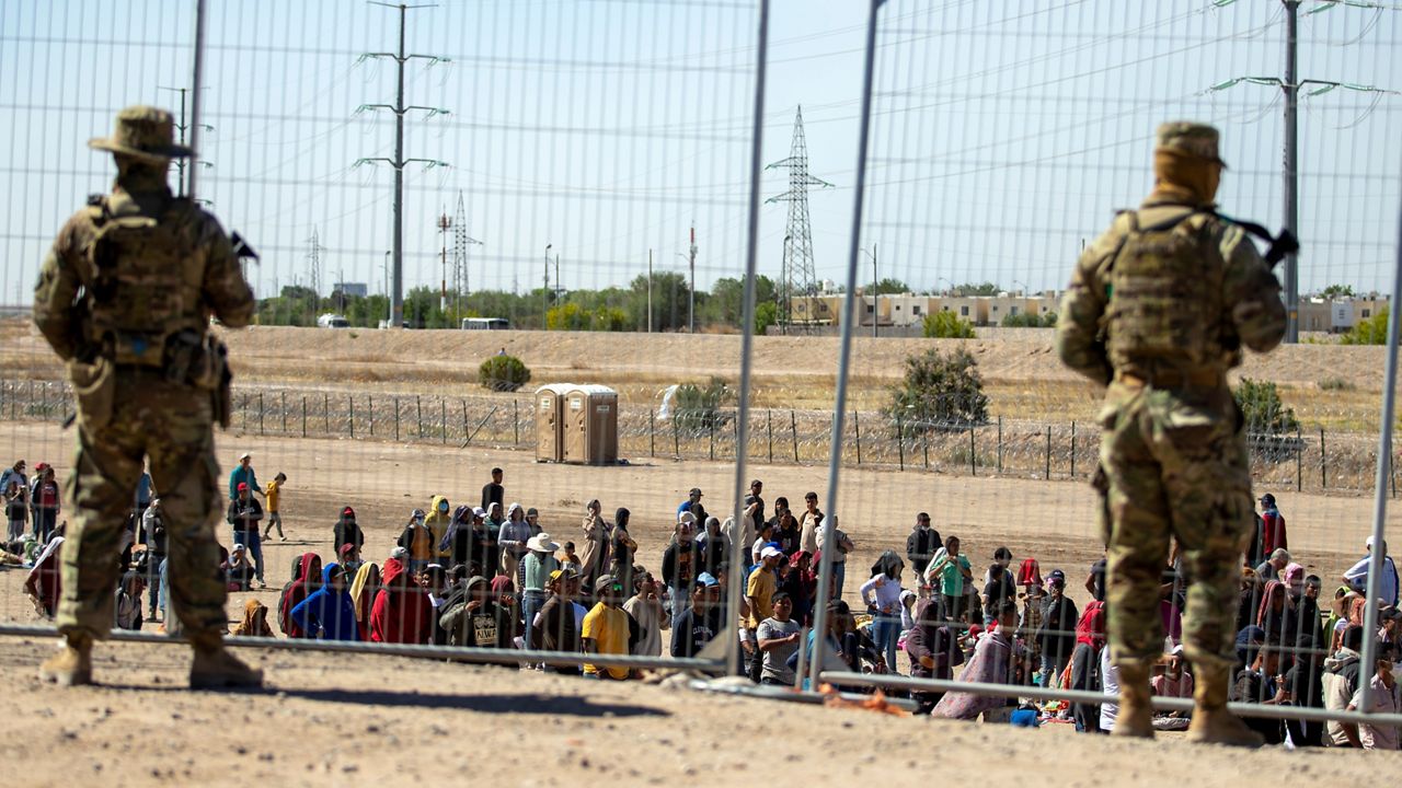 Migrants wait in line adjacent to the border fence under the watch of the Texas National Guard to enter into El Paso, Texas, May 10, 2023. 