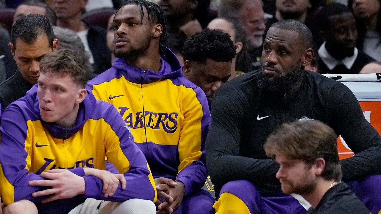 Los Angeles Lakers guard Bronny James, center, and forward LeBron James, right, watch from the bench with guard Dalton Knecht, left, in the first half of an NBA basketball game against the Cleveland Cavaliers, Wednesday, Oct. 30, 2024, in Cleveland. (AP Photo/Sue Ogrocki)