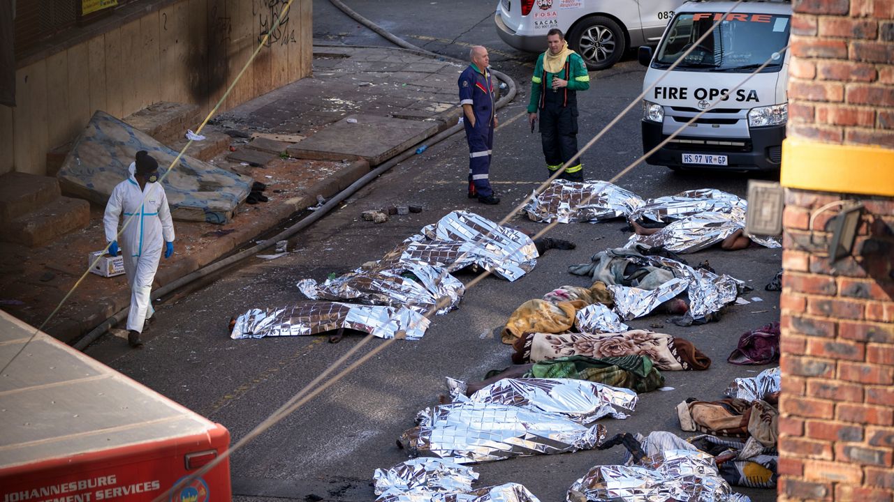 Medics stand by the covered bodies of victims of a deadly blaze in downtown Johannesburg, Thursday, Aug. 31, 2023. Dozens died when a fire ripped through a multi-story building in Johannesburg, South Africa's biggest city, emergency services said Thursday. (AP Photo/Jerome Delay)