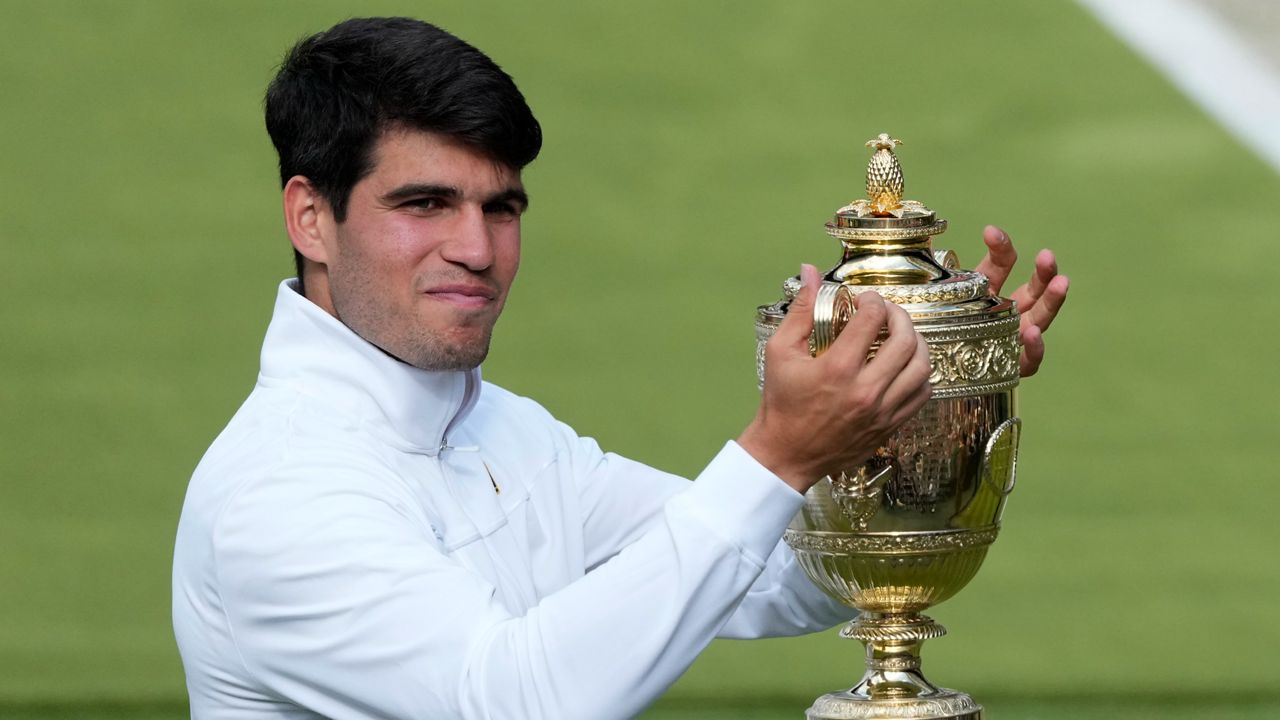 Carlos Alcaraz of Spain smiles as he holds up his trophy for the photographers after defeating Novak Djokovic of Serbia in the men's singles final at the Wimbledon tennis championships in London, Sunday, July 14, 2024. (AP Photo/Mosa'ab Elshamy)