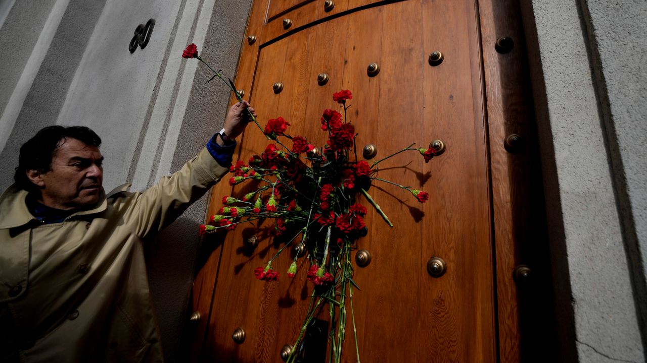 The relative of a person who was executed during Chile's dictatorship places a flower on the east side door of La Moneda presidential palace, through which the body of President Salvador Allende was carried by soldiers and firefighters 50 years ago after the military coup that toppled his government in Santiago, Chile, Monday, Sept. 11, 2023. (AP Photo/Esteban Felix)