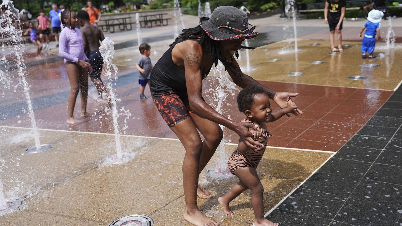 Shanae Brooks cools off with her daughter, Devynn, 2, at a splash pad Friday, June 20, 2025, in Cincinnati. (AP Photo/Joshua A. Bickel)
