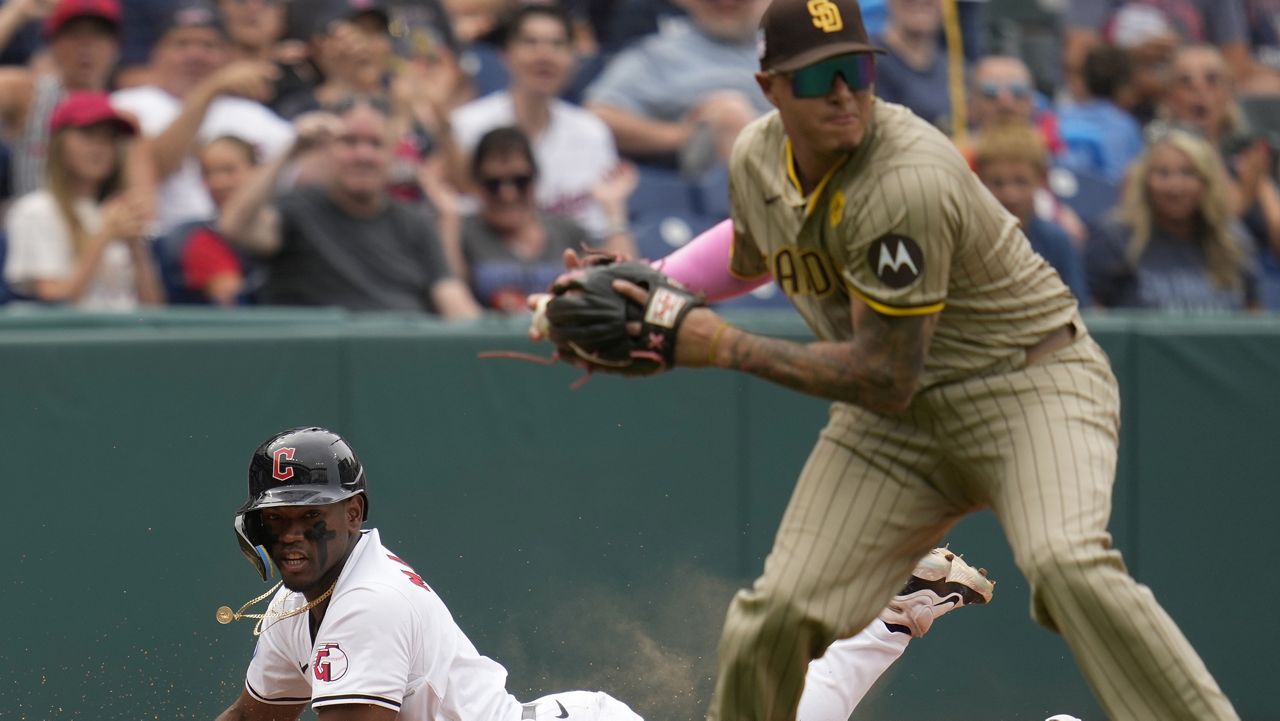 Cleveland Guardians' Angel Martínez, left, slides safely into third base as San Diego Padres third baseman Manny Machado, right, throws to second base for an out against Guardians' José Ramírez in the seventh inning of a baseball game Sunday, July 21, 2024, in Cleveland. (AP Photo/Sue Ogrocki)