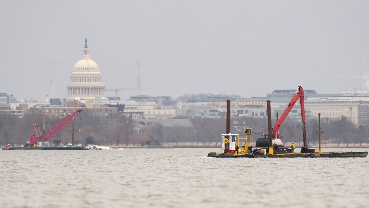 With the U.S. Capitol in the background, cranes are pictured in the Potomac River on Sunday, Feb. 2, 2025, near the wreckage of an American Airlines jet, at left, that collided midair with an Army Black Hawk helicopter in Arlington, Va., as seen from Alexandria, Va. (AP Photo/Carolyn Kaster)