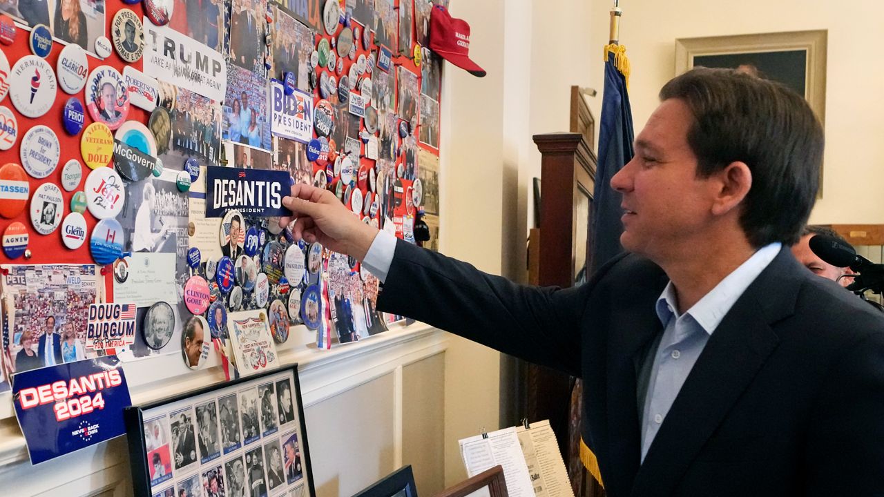 Republican presidential candidate and Florida Gov. Ron DeSantis puts a campaign sticker on a wall featuring current and past presidential candidates while visiting to file papers to be on the New Hampshire Republican Primary ballot at the New Hampshire State House, Thursday, Oct. 12, 2023, in Concord, N.H. (AP Photo/Charles Krupa)