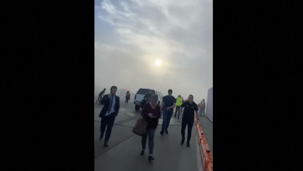 In this image taken from video provided by Justus Rainey, passengers move away from a plane as smoke surrounded the aircraft, in Denver, Thursday, March 13, 2025. (Justus Rainey via AP)