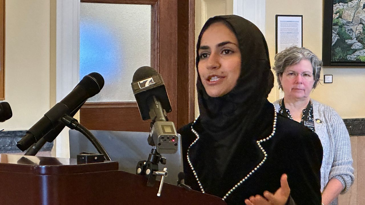 Eisha Khan, a member of the Maine Permanent Commission on the Status of Women, talks about economic instability faced by many women Thursday in the State House Hall of Flags. (Spectrum News/Susan Cover)