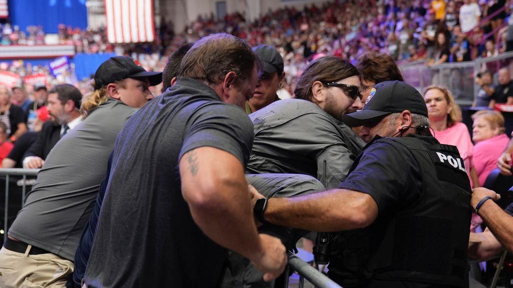 Police remove a man, center with sunglasses, who had climbed onto the media riser, as Republican presidential nominee former President Donald Trump speaks at a campaign event, Friday, Aug. 30, 2024, in Johnstown, Pa. (AP Photo/Alex Brandon)