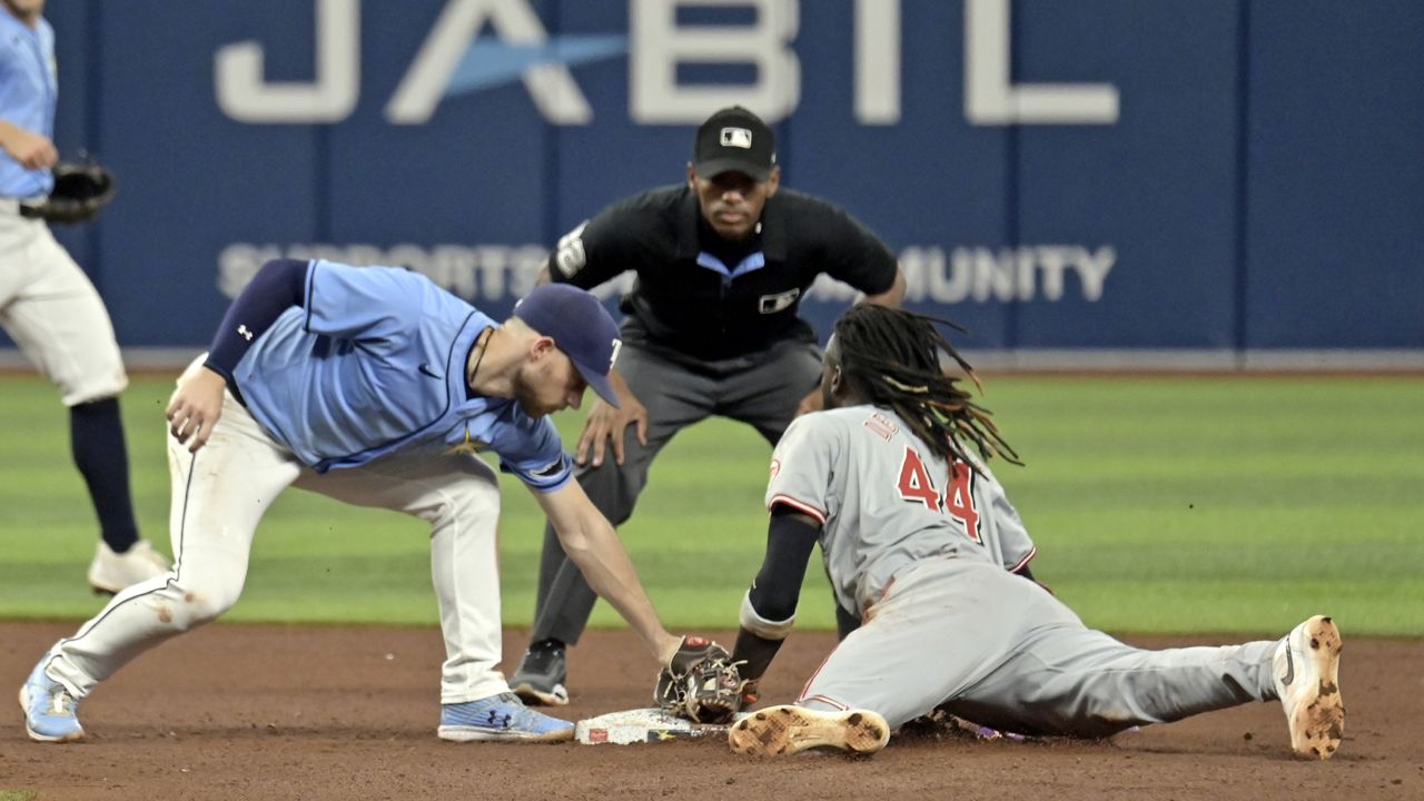 Tampa Bay Rays shortstop Taylor Walls, left, and umpire Edwin Moscoso, center, watch as Cincinnati Reds' Elly De La Cruz (44) bats the tag from Brandon Lowe for a stolen base during the sixth inning of a baseball game, Sunday, July 28, 2024, in St. Petersburg, Fla. (AP Photo/Steve Nesius)