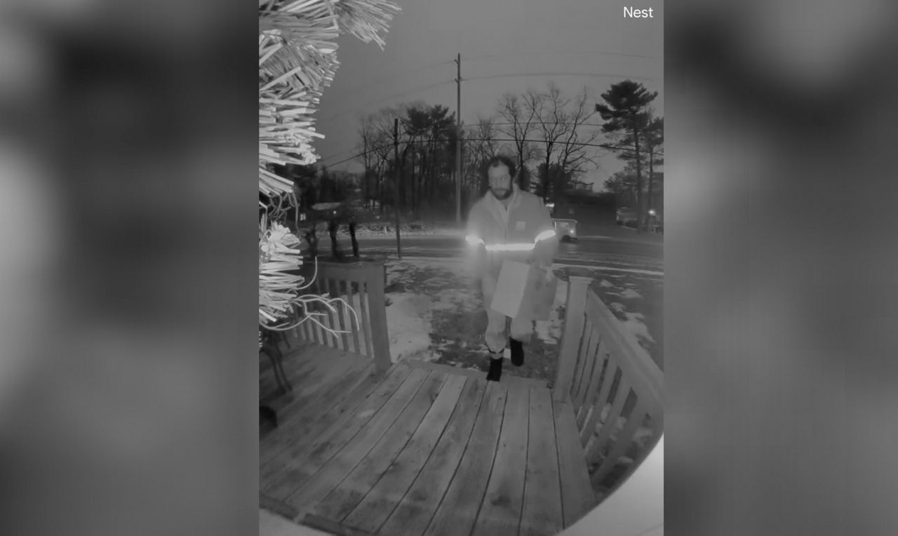 Mailman delivers a box to the front door of a porch.