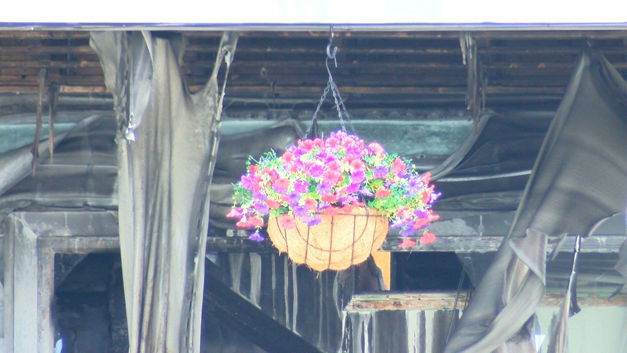 A basket of flowers hangs in front of the charred entrance to the Gabriel House Assisted Living Facility on Monday. (Spectrum News 1/Devin Bates) 