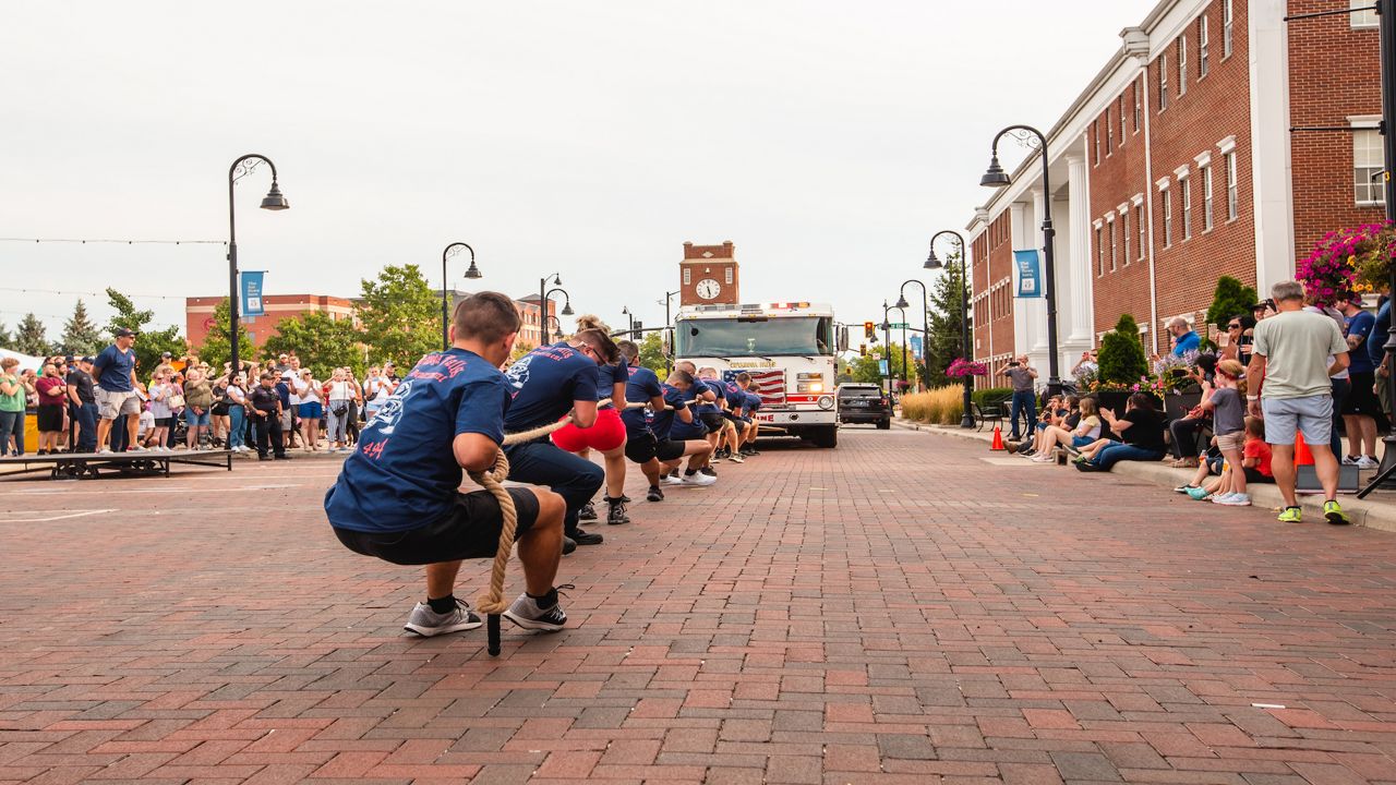 people pulling fire truck with a rope on a brick street