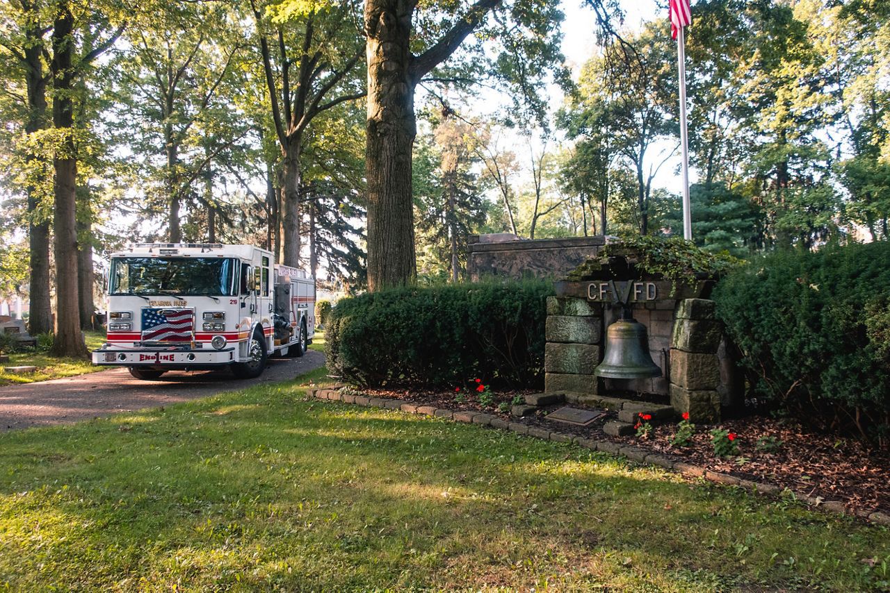 a fire truck in a cemetery near a memorial with a large bell