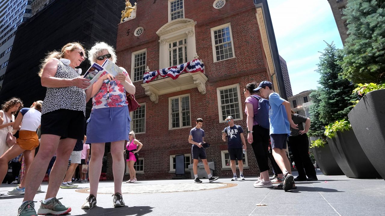 Cathy Nau, front left, and Jackie Trimble, front second left, both of Lake Stevens, Wash., examine maps, Wednesday, July 3, 2024, in front of the Old Statehouse, in Boston. (AP Photo/Steven Senne)