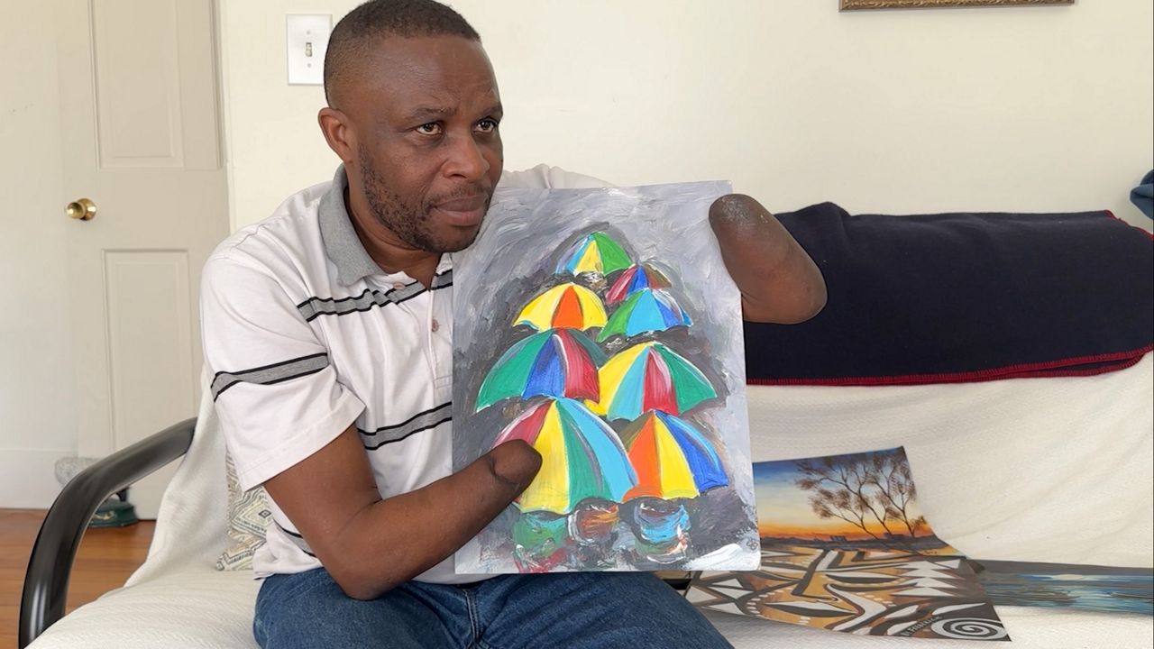 Frederick Ndabaramiye, 41, a native of Rwanda, now an artist living in Portland, shows off one of his latest works of acrylic paints on paper. He said the piece was less about painting umbrellas, and more about an excuse to paint in bright colors. (Spectrum News/Sean Murphy)