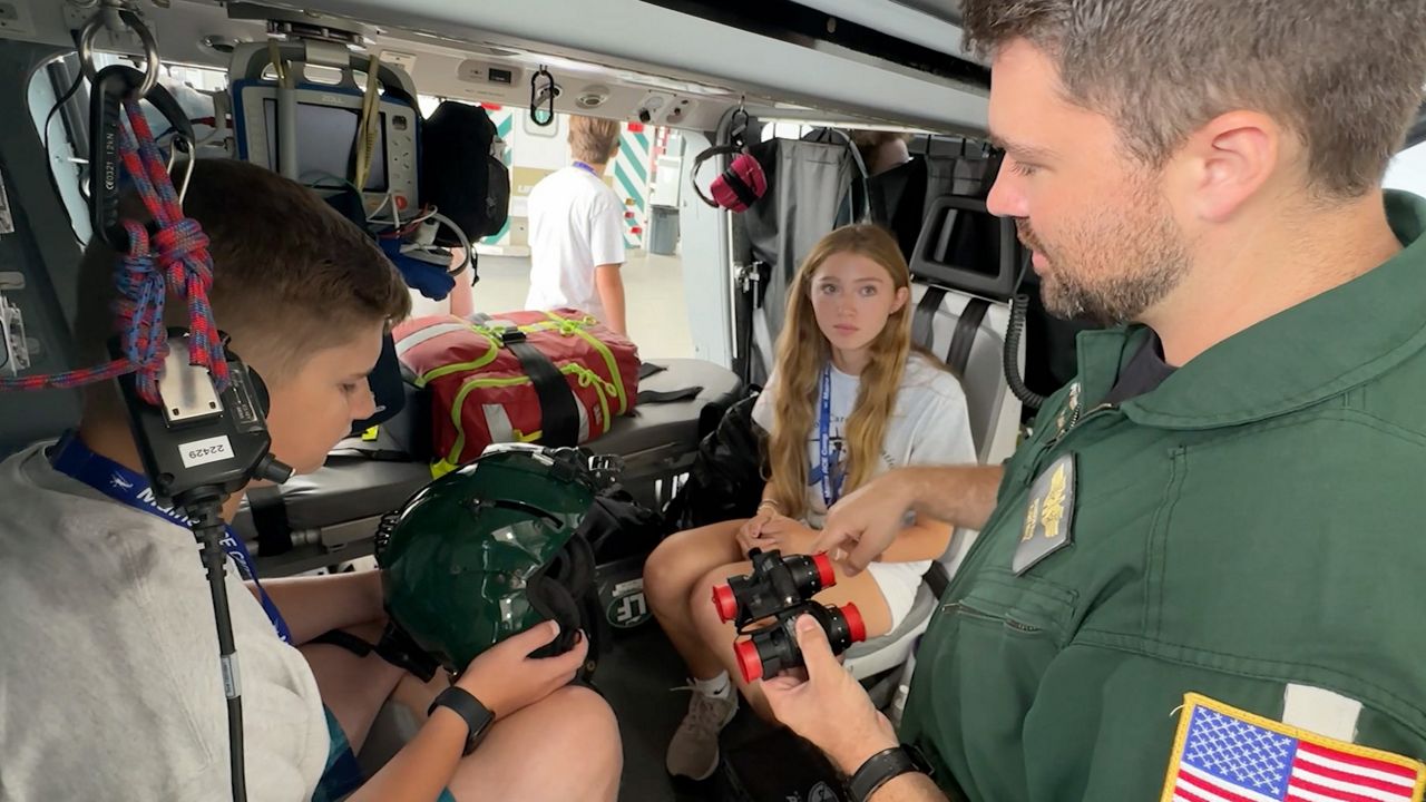 Brandon Mayo, right, a nurse with Lifeflight of Maine, shows a pair of night-vision goggles to Gavin Dusza, 13, right, and Avery Turner, 14 at Sanford Airport Wednesday. The students were part of the annual ACE Camp, which aims to inspire young people to pursue careers in aviation. (Spectrum News/Sean Murphy)