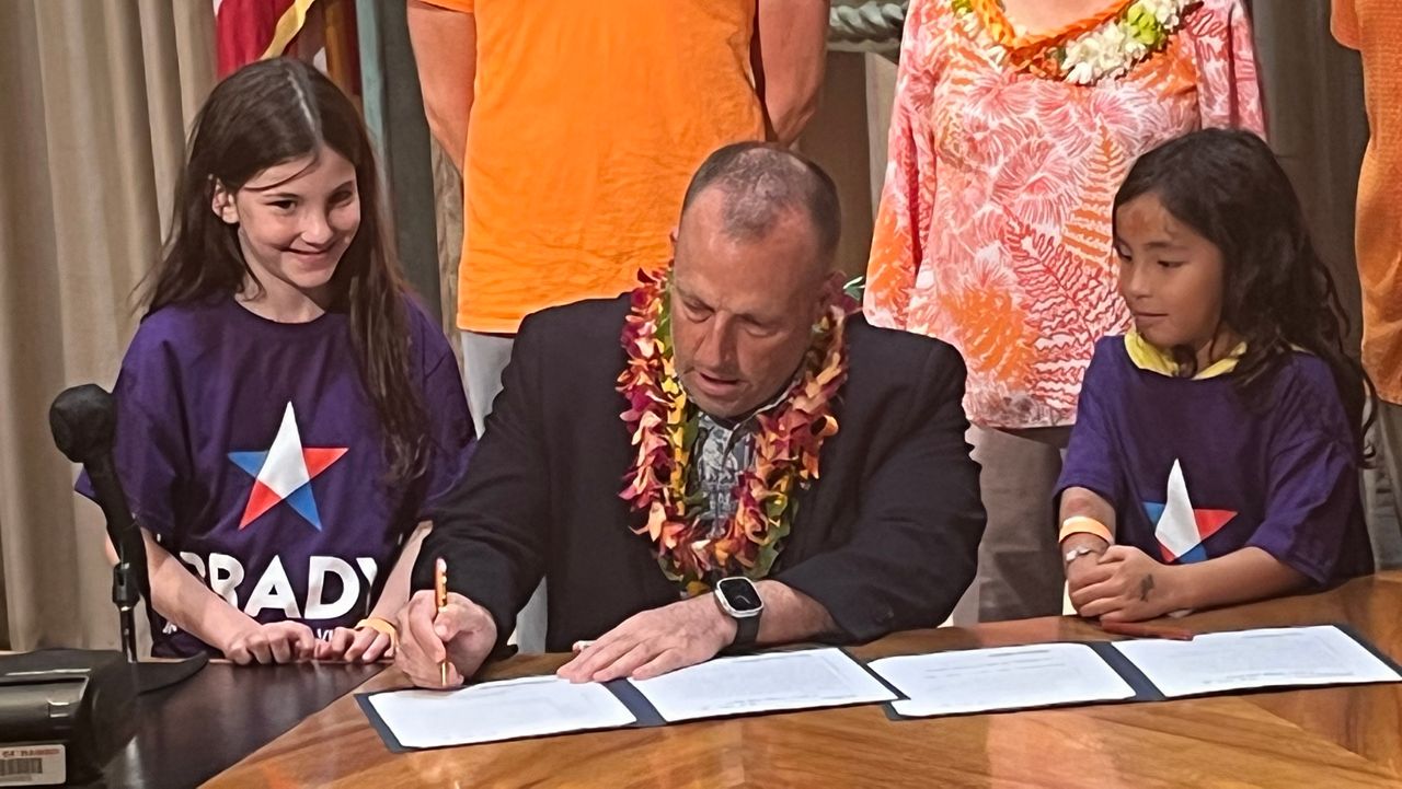 Flanked by two young representatives of the Brady Center to Prevent Gun Violence, Gov. Josh Green signed a pair of bills that address concealed carry of firearms and active-shooter training. (Spectrum News/Michael Tsai)