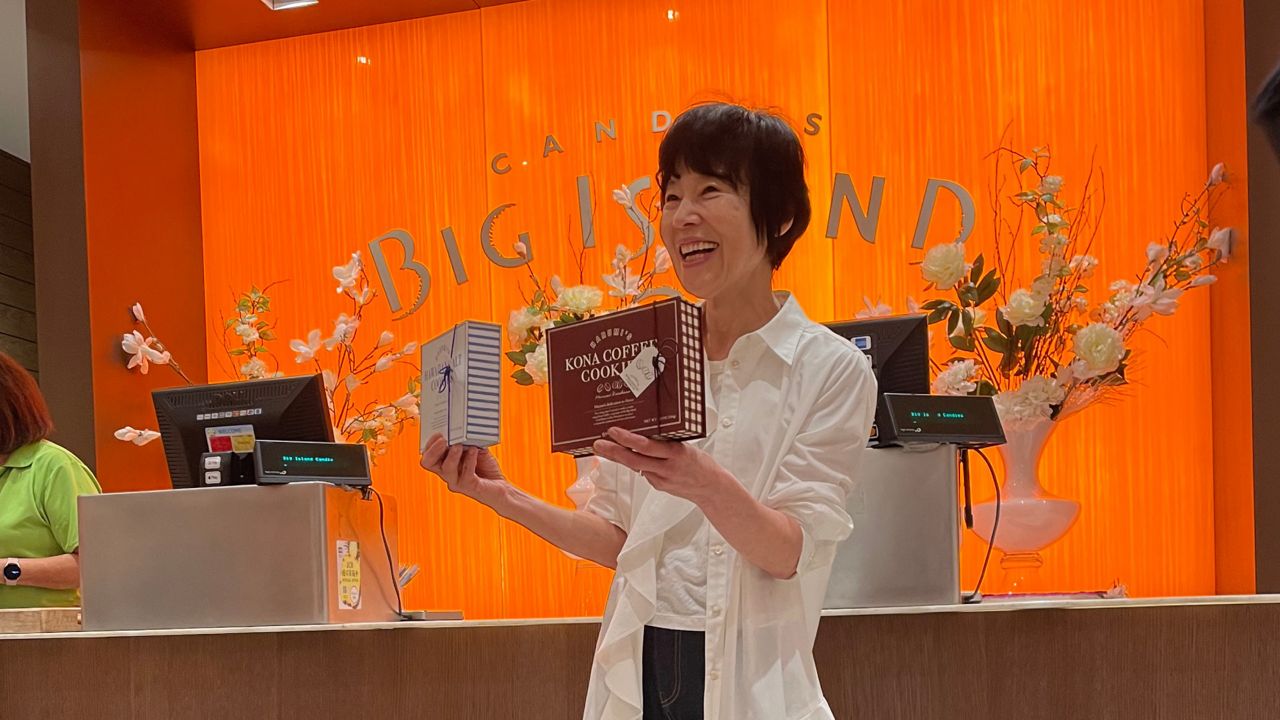 Harumi Kurihara poses with her two signature offerings — Hawaiian Salt Cookies, and her new Kona Coffee Cookies — at Big Island Candies' Ala Moana Center store. (Spectrum News/Lianne Bidal Thompson)