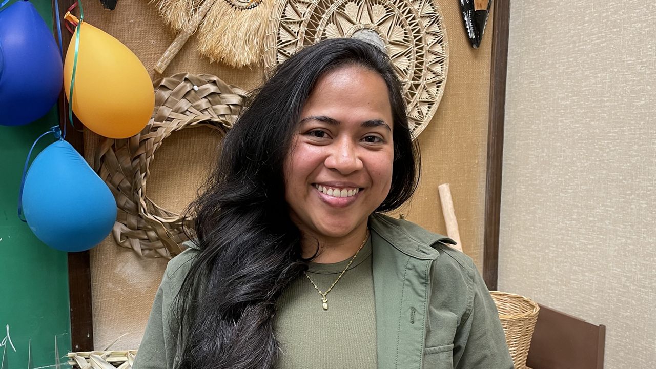Carol Ann Carl stands in her office at the University of Hawaii at Manoa with Micronesian treasures, including a Chuukese mask and a Marshallese handicraft, hung up behind her. (Michelle Broder Van Dyke/Spectrum News) 