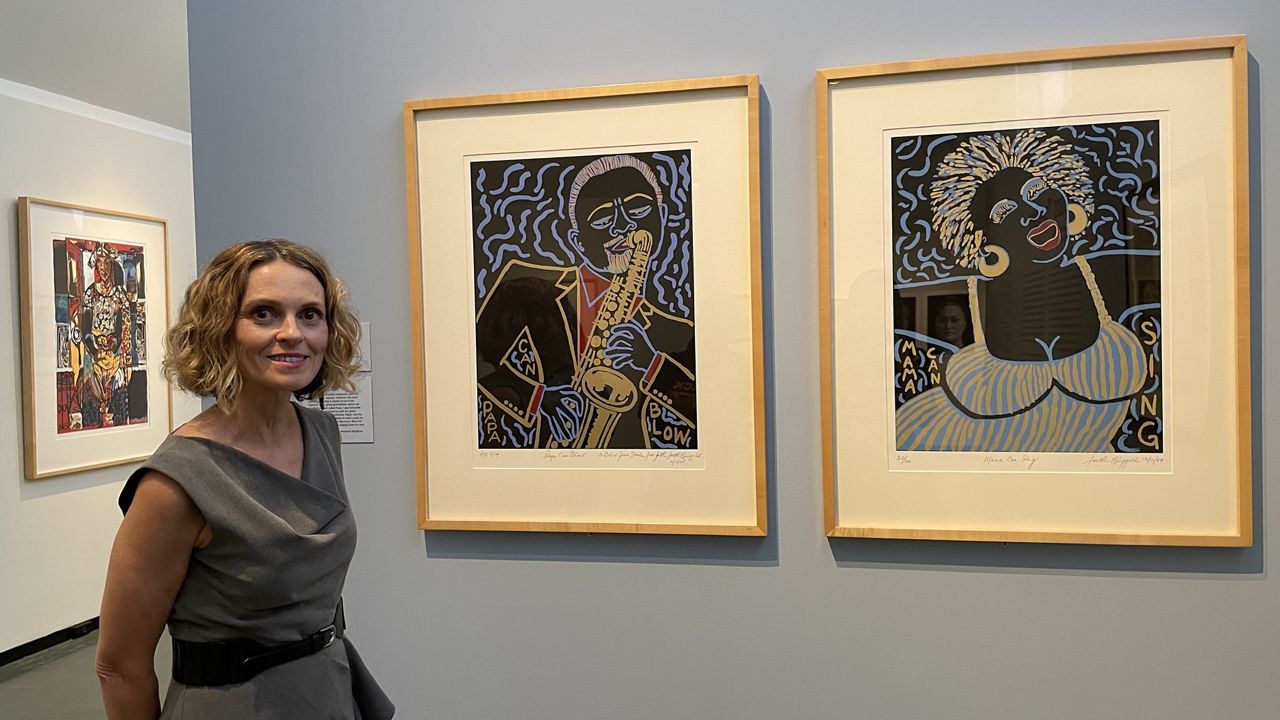 Katherine Love stands next to Faith Ringgold’s “Papa Can Blow” (2005) and  “Mama Can Sing” (2004), which are part of the "Forward Together" exhibit. (Spectrum News/Michelle Broder Van Dyke)