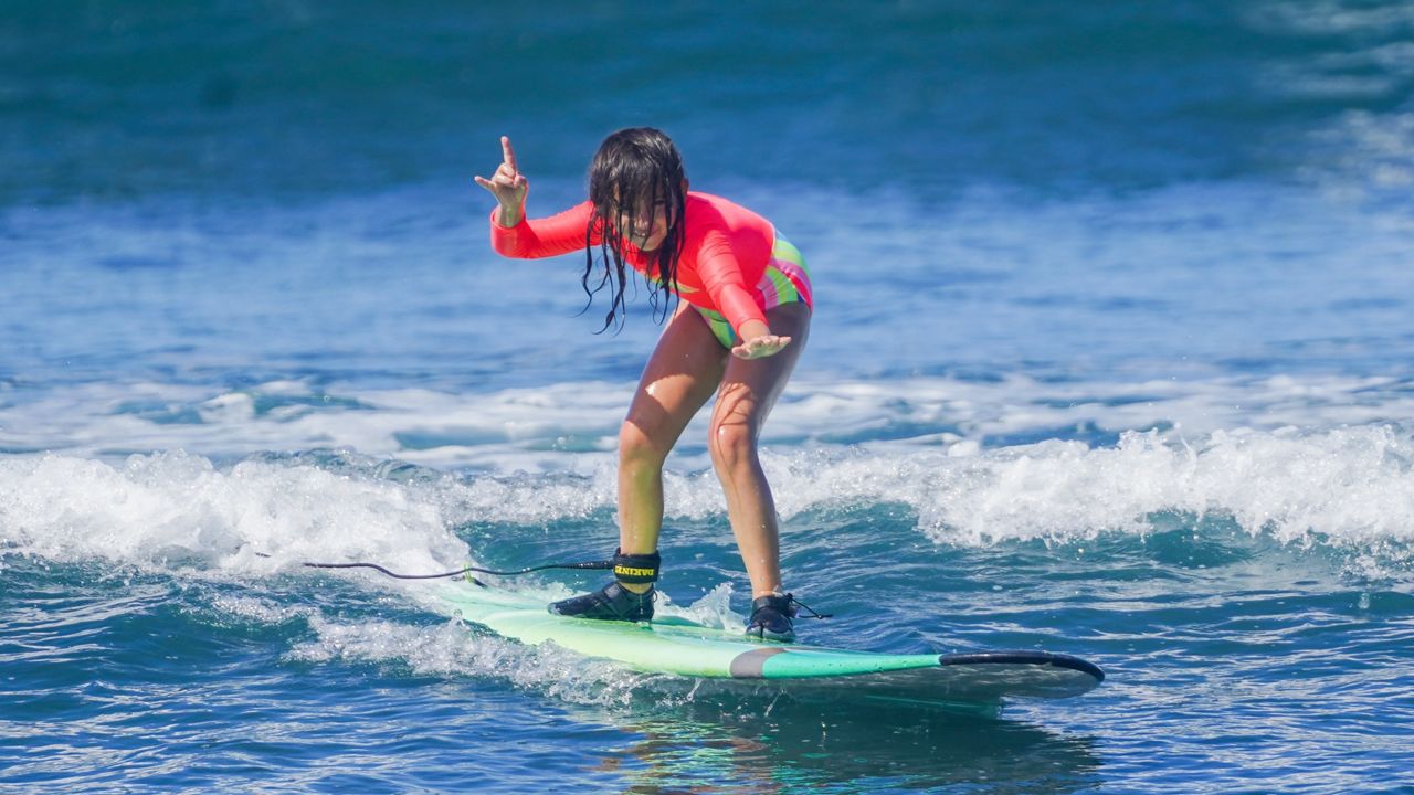 A young girl catches a wave while attending a Maui Surfer Girls surf camp. (Photo courtesy of Dustin Tester)