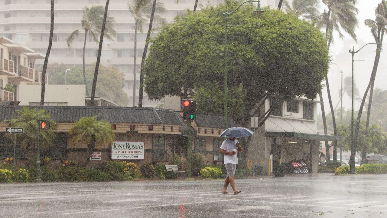 A man uses an umbrella against the rain as he walks across Kapiolani Blvd in Waikiki in Honolulu on Friday, Aug. 8, 2014. (AP Photo/Marco Garcia)