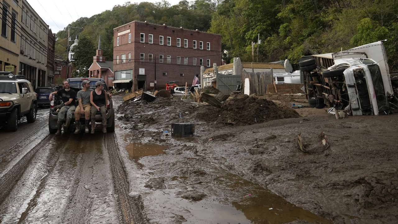 People ride in the back of a pickup truck on a mud-covered street left in the aftermath of Hurricane Helene, Tuesday, Oct. 1, 2024, in Marshall, N.C. (AP Photo/Jeff Roberson)