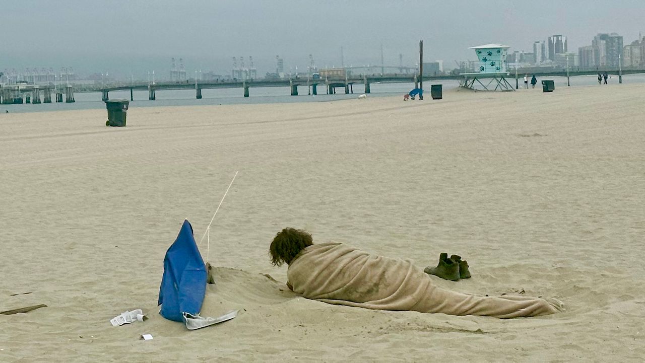 A homeless man sleeps on the beach in Belmont Shore, Long Beach, Calif. (Spectrum News/Joseph Pimentel)