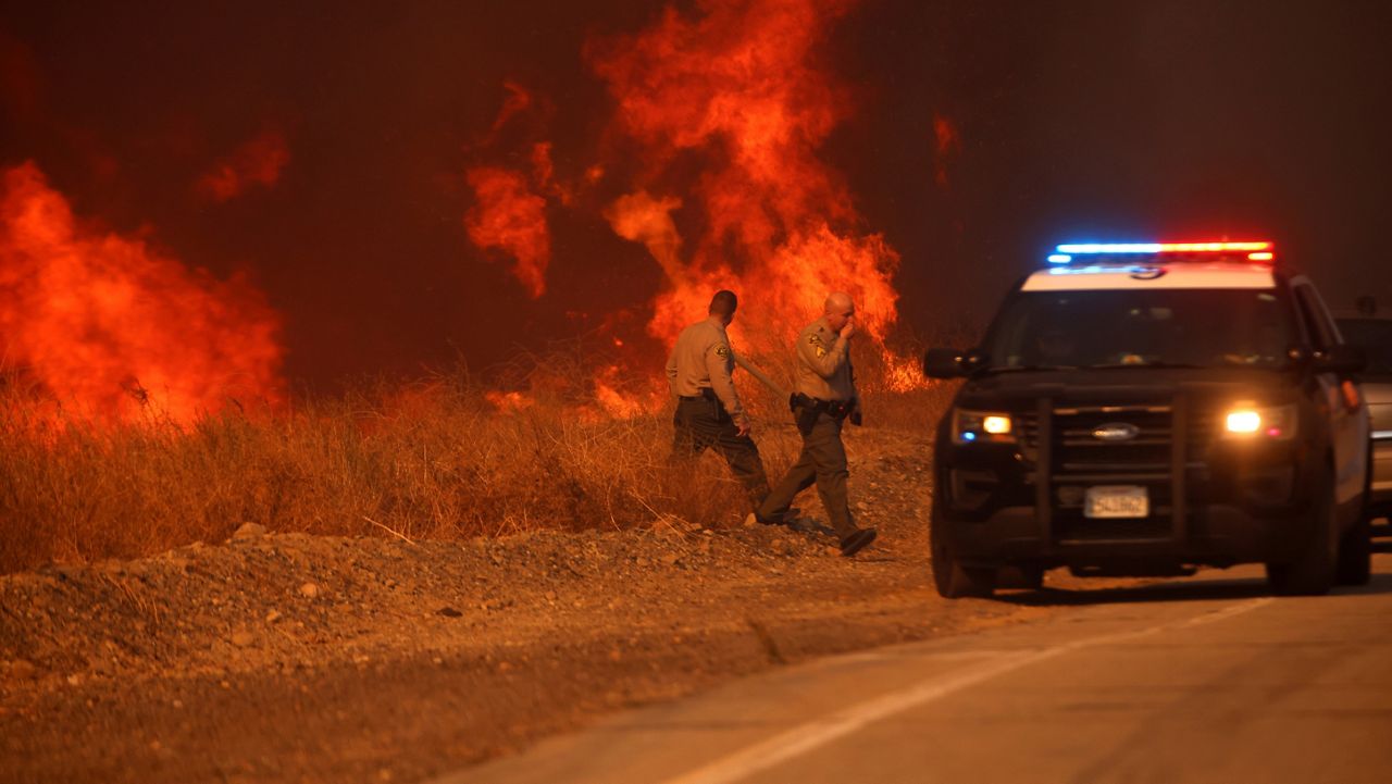 County Sheriff officers return to their vehicle after monitoring flames caused by the Hughes Fire along a roadside in Castaic, Calf., Wednesday, Jan. 22, 2025. (AP Photo/Ethan Swope)