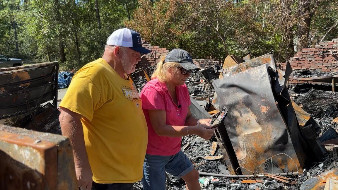 Doug and Debbie Sherwood look through ruined photos together in what's left of their home of 23 years. (Spectrum News 1/Rachel Boyd)