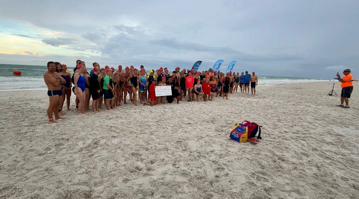 Clearwater Beach Lifeguards pose with a check for the nearly $5,000 the Ocean Mile Swim raised for Tampa Bay Crisis Center. (Spectrum News)