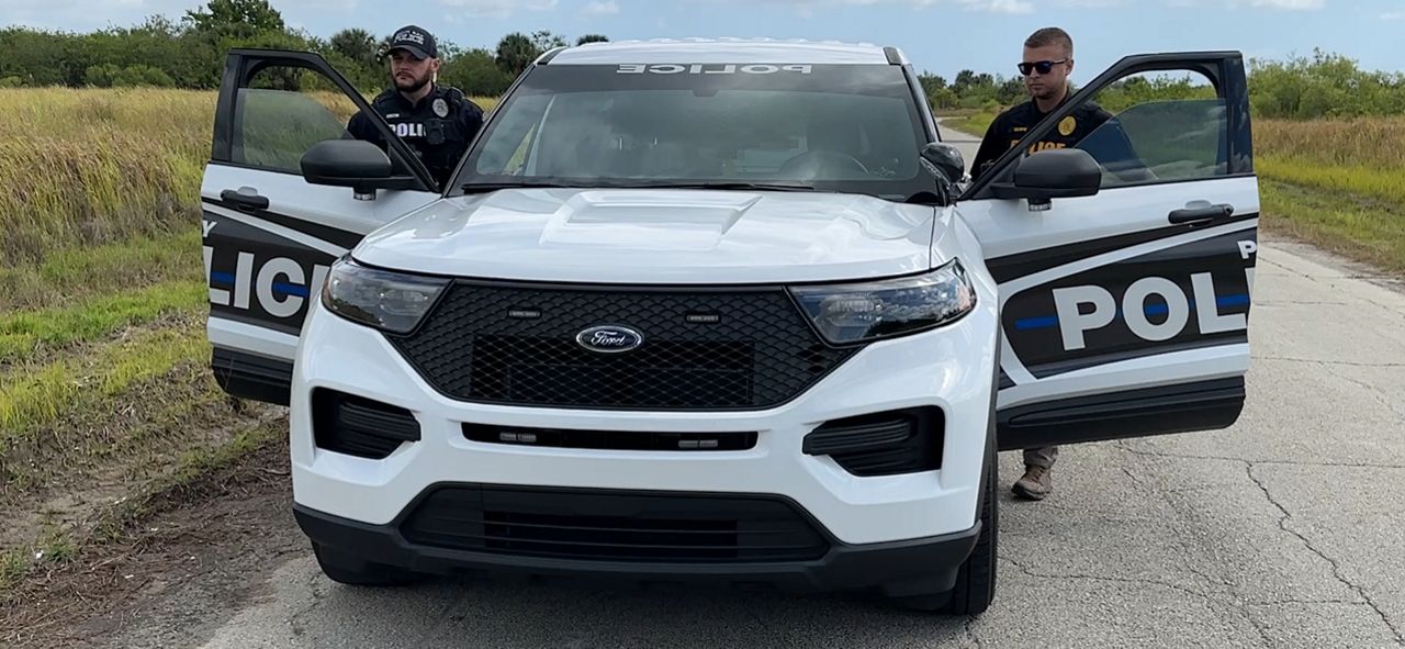 Two Palm Bay police officers stand outside their patrol vehicle in The Compound. (Spectrum News)