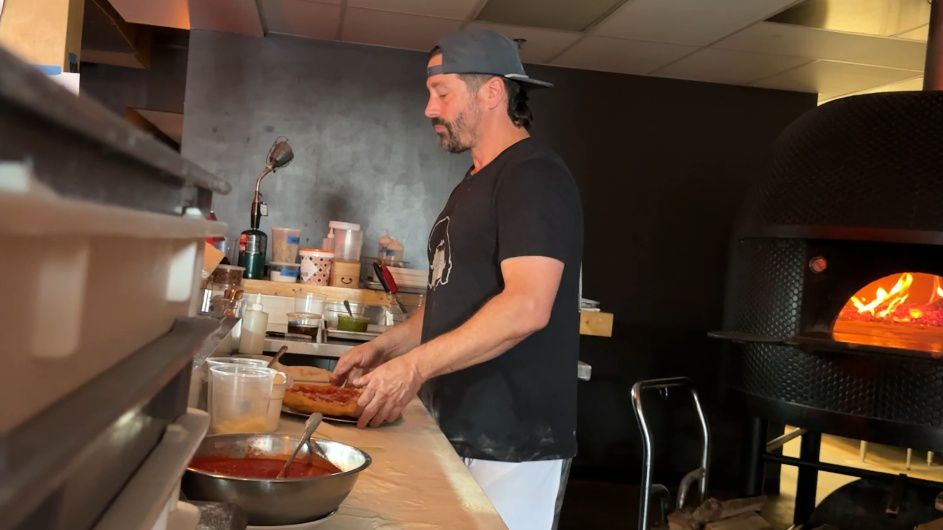 Peyton Smith crafting a pizza in his kitchen.