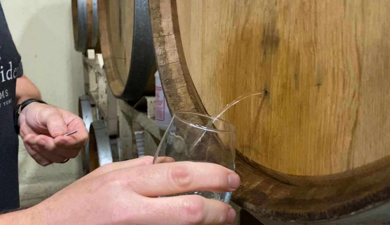 A man takes a sample of cider from a barrel. 