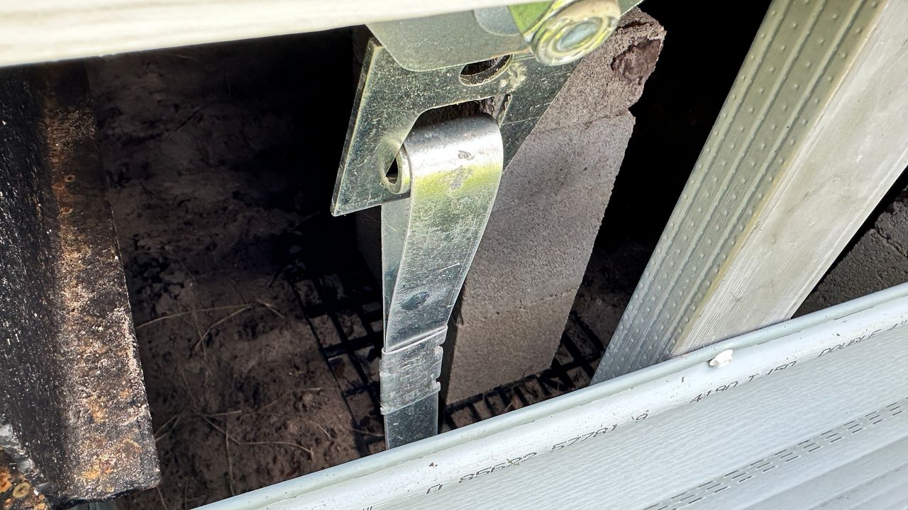A metal strap tie-down is connected to the frame of a Palm Harbor area manufactured home and an auger a few feet into the ground. (Spectrum Bay News 9/Josh Rojas)