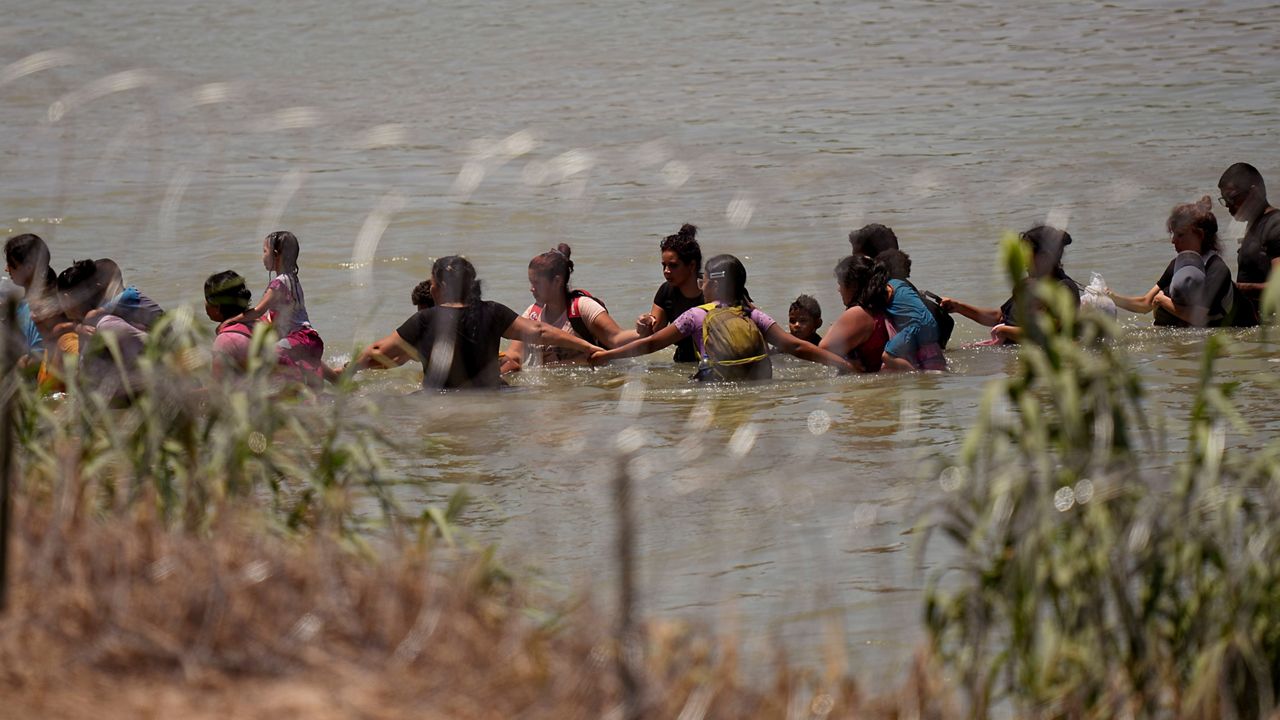 Migrants join hands as they cross the Rio Grande near the site where large buoys are being deployed to be used as a border barrier in Eagle Pass, Texas, Wednesday, July 12, 2023. (AP Photo/Eric Gay)