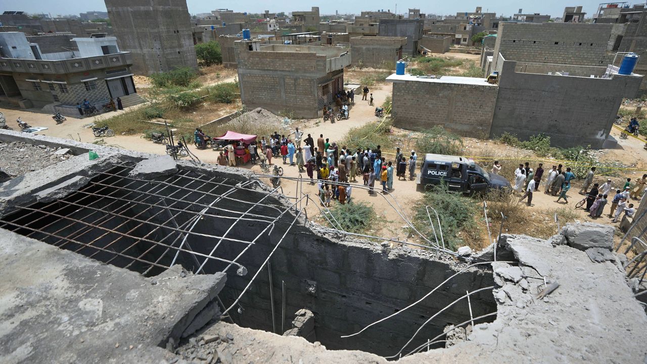 A big hole is seen on a rooftop of a house suspected to have been damaged in Indian drone attack as residents, behind, gather near a cordoned off site, where Pakistan's air defense system shot down a suspected Indian drone in Karachi, Pakistan, Thursday, May 8, 2025. (AP Photo/Fareed Khan)