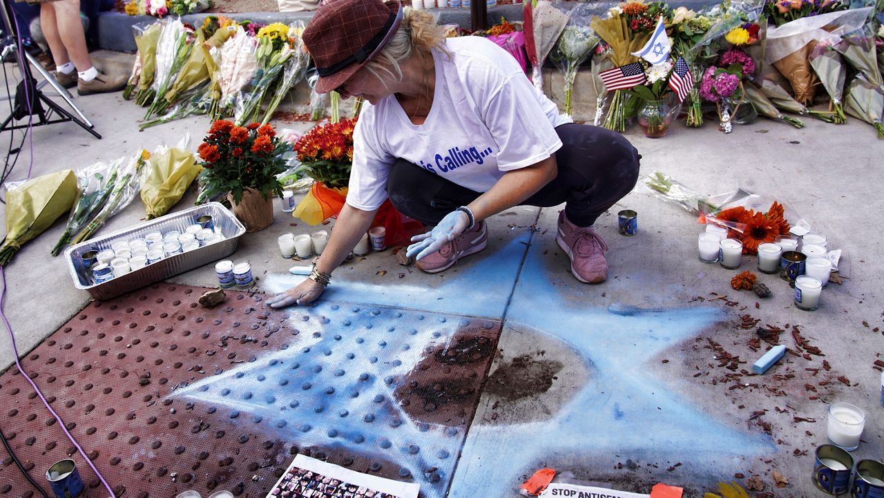 Elena Colombo chalks a Star of David amongst flowers and candles left at a makeshift shrine placed at the scene of a Sunday confrontation that lead to death of a demonstrator Tuesday, Nov. 7, 2023, in Thousand Oaks, Calif. (AP Photo/Richard Vogel)