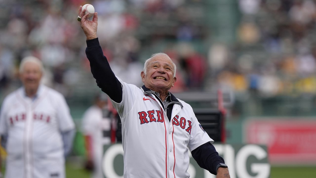 Joe Castiglione, left, radio voice of the Boston Red Sox since 1983, throws out a ceremonial first pitch during pregame ceremonies for Castiglione, before the Tampa Bay Rays played the Red Sox in a baseball game, Sunday, Sept. 29, 2024, in Boston. (AP Photo/Steven Senne)