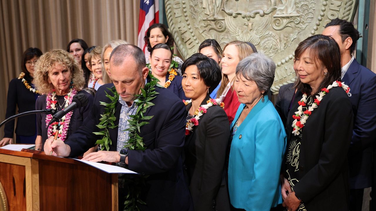 Nanci Kriedman, left, outgoing CEO of the Domestic Violence Action Center, looks on as Gov. Josh Green signs one of several a domestic violence measures.(Office of Gov. Josh Green)