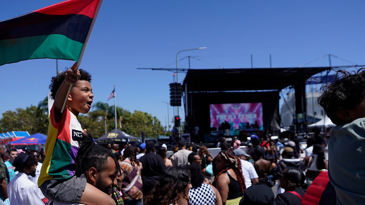 Julien James carries his son, Maison, 4, holding a Pan-African flag, to celebrate during a Juneteenth commemoration at Leimert Park in Los Angeles on June 18, 2022.