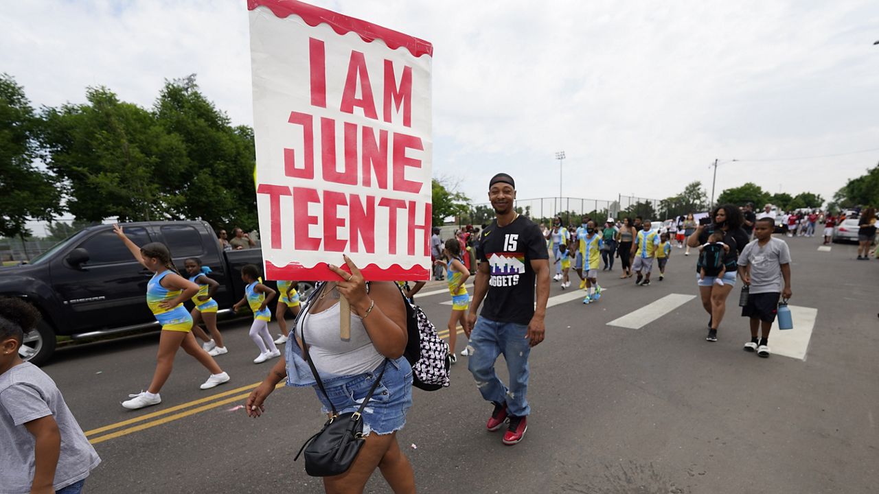 A woman carries a sign during a parade to mark Juneteenth on Saturday, June 19, 2021, in Denver. (AP Photo/David Zalubowski)