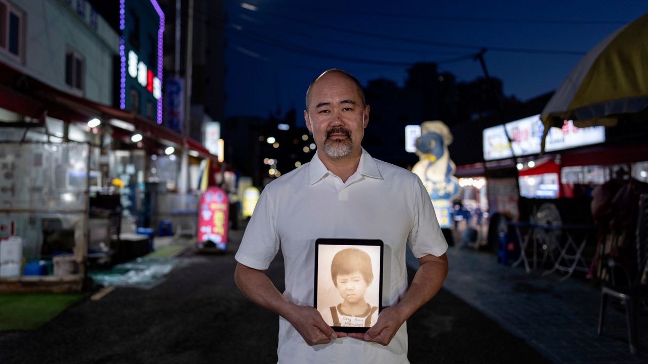 Kenneth Barthel, adopted from South Korea to Hawaii in 1979 at 6 years old, holds a tablet showing his childhood photo in Busan, South Korea, Thursday, May 16, 2024. Barthel is looking for his birth family in Busan where he believes he was abandoned when his mother ordered soup for him in a restaurant and never returned. (AP Photo/Jae C. Hong)