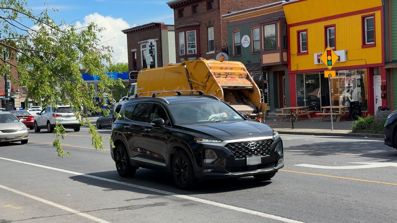 Cars with objects on rearview mirrors are driving in Albany, NY.