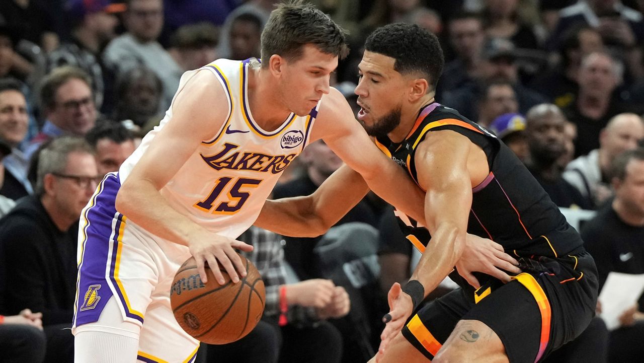 Los Angeles Lakers guard Austin Reaves (15) shields the ball from Phoenix Suns guard Devin Booker during the first half of an NBA basketball game, Tuesday, Nov. 26, 2024, in Phoenix. (AP Photo/Rick Scuteri)