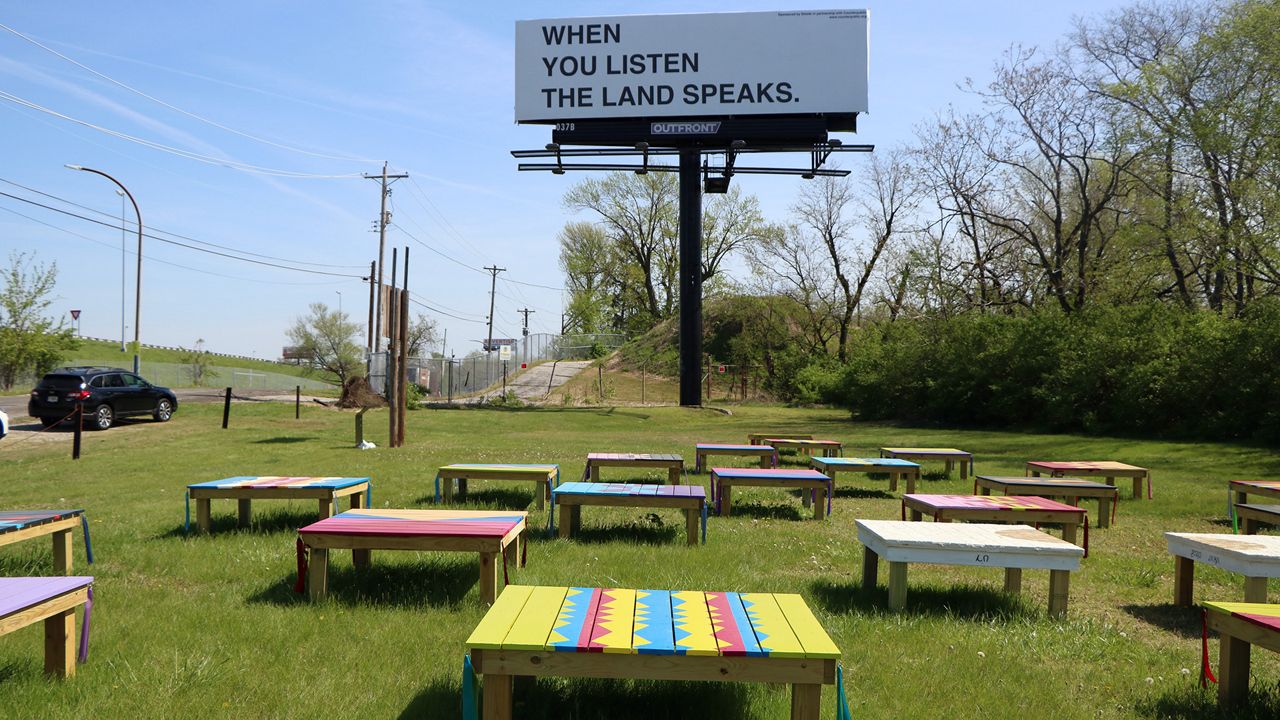 Anita and Nokosee Fields created 40 wooden platforms called "Wayback" that are painted and embellished with ribbons, tile and sound. The billboard called "Give it Back: Stage Theory" was created by New Red Order. The art pieces are near Sugarloaf Mound, which is the last and oldest remaining human-made mound by Native Americans in St. Louis. (Spectrum News/Elizabeth Barmeier)