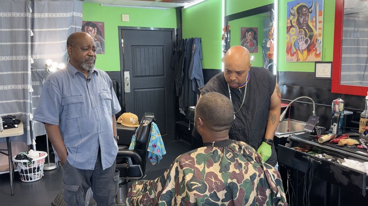 Larry Hester watching his son cut hair in his Durham barber shop.