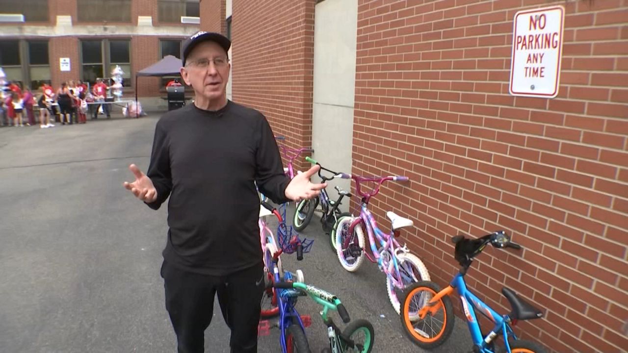Larry the bike man speaks next to a number of children's bikes by the side of a building