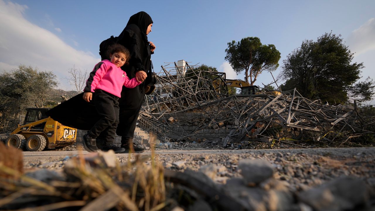 A woman with a child pass at the site where an Israeli airstrike hit a house in Aalmat village, northern Lebanon, Sunday, Nov. 10, 2024. (AP Photo/Hassan Ammar)